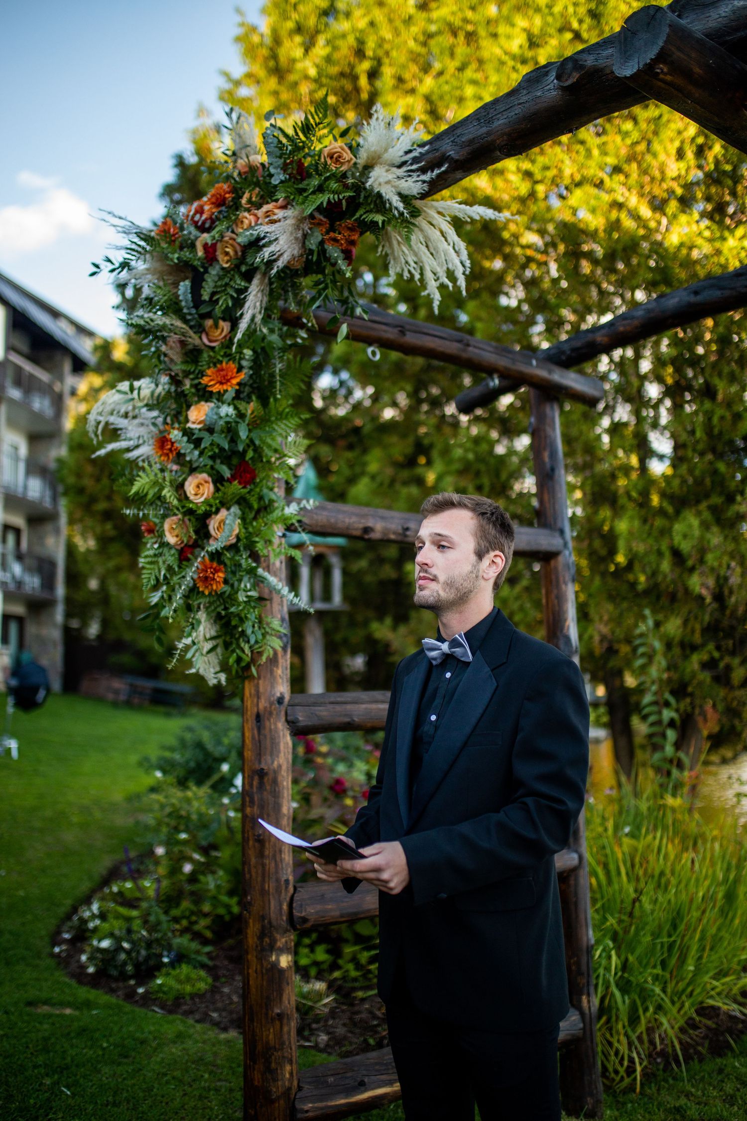 A person in a black coat stands under a wooden pergola decorated with holiday greenery and lights.