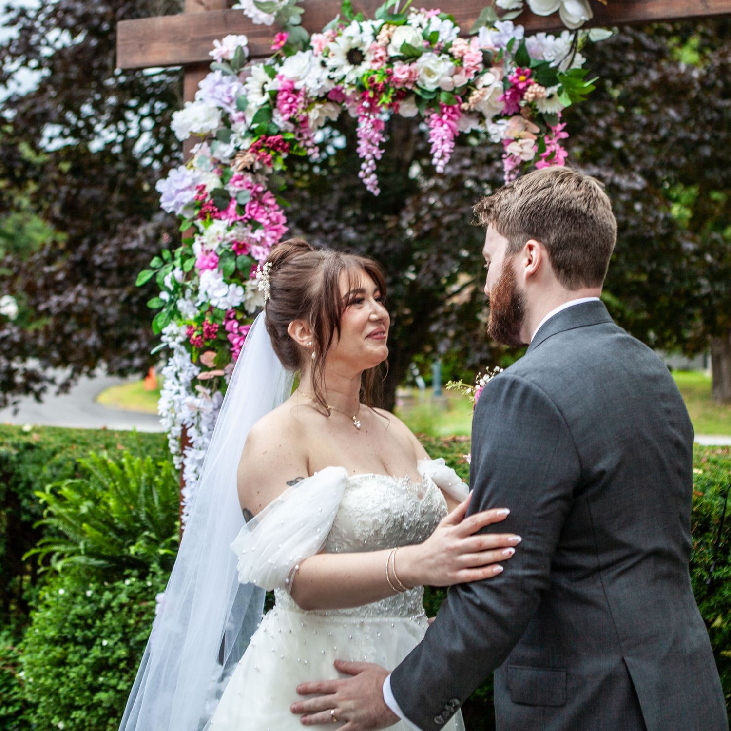 A couple shares an intimate moment under a floral arch at their outdoor wedding.