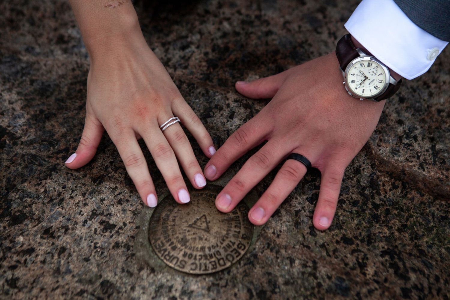Close-up of hands displaying wedding rings on rustic stone surface.