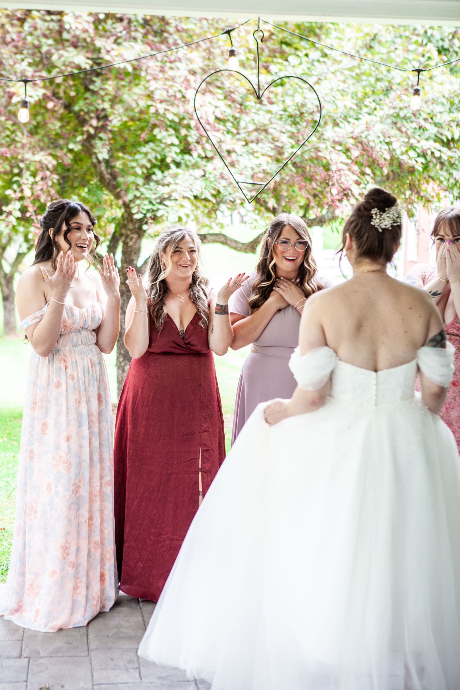 Wedding party poses outdoors in pink and burgundy dresses under blooming trees.