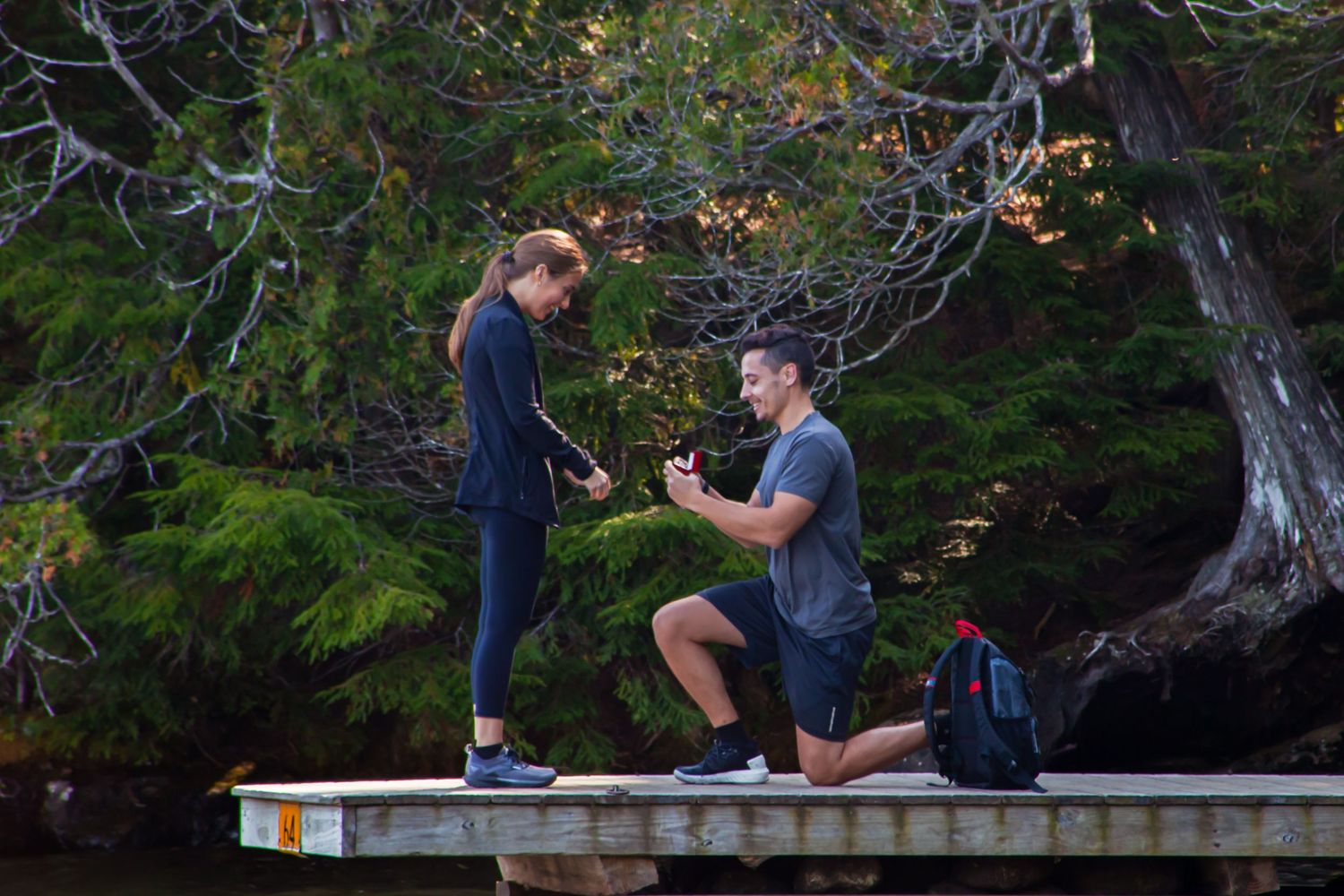 A couple shares an intimate moment on a stone wall surrounded by trees during sunset.