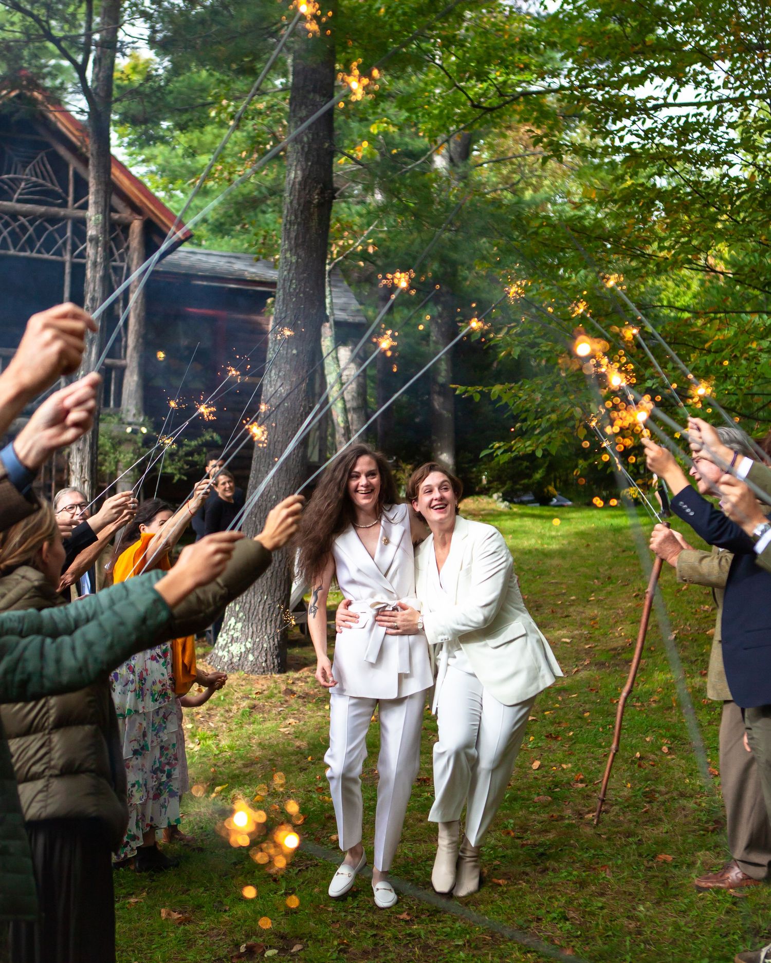Wedding guests hold sparklers creating a magical light display in an outdoor garden setting.