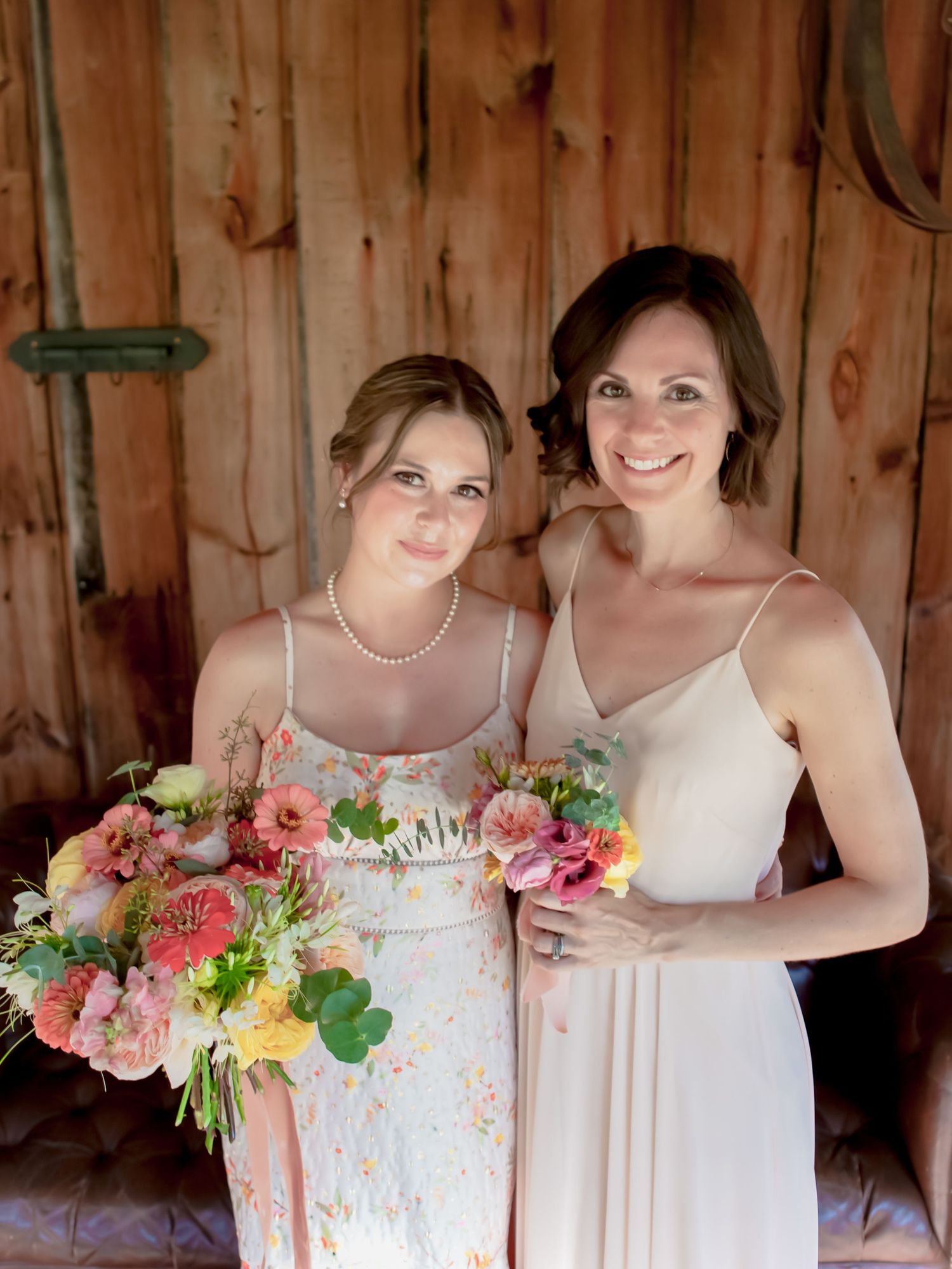 Bridesmaids in light pink dresses holding colorful bouquets inside rustic barn setting.