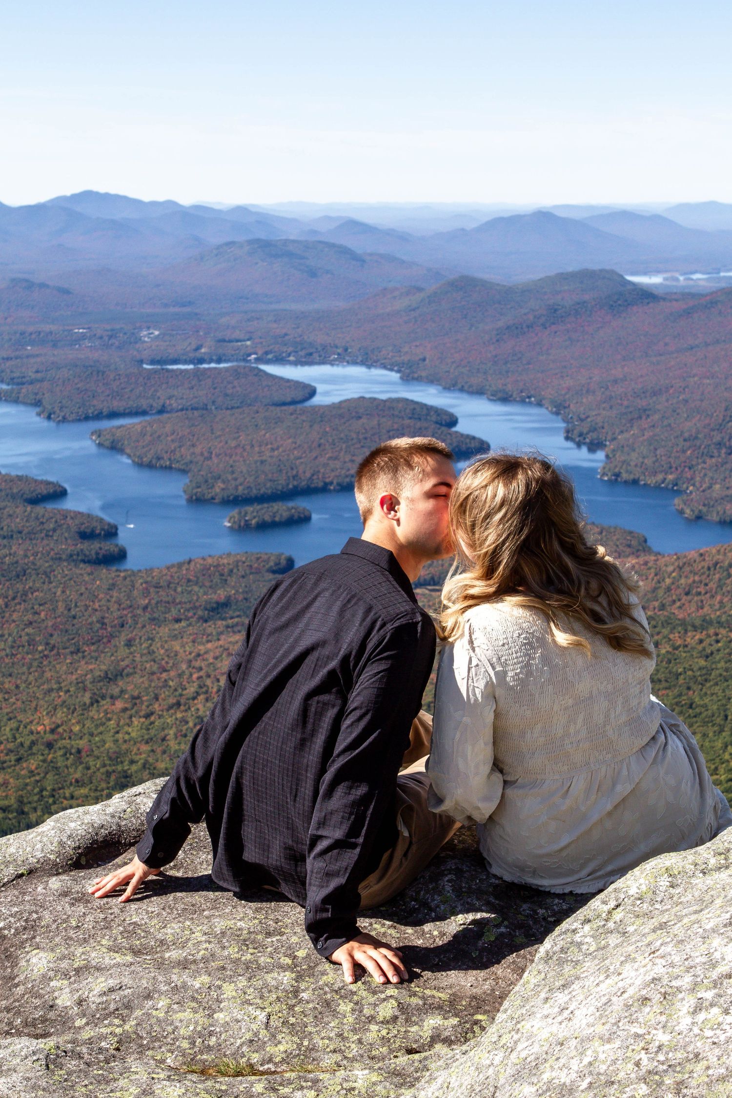 Couple kissing on a rocky mountain summit overlooking Lake Placid and colorful autumn foliage in the Adirondacks.