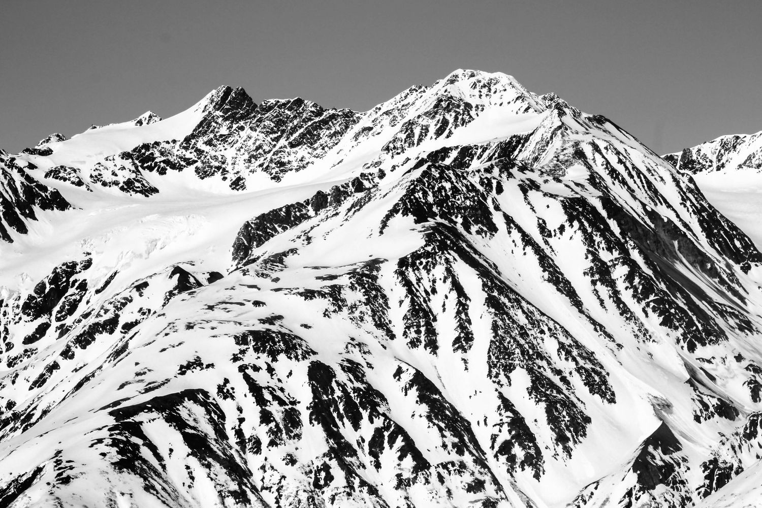 A dramatic black and white panorama of snow-capped mountain peaks.