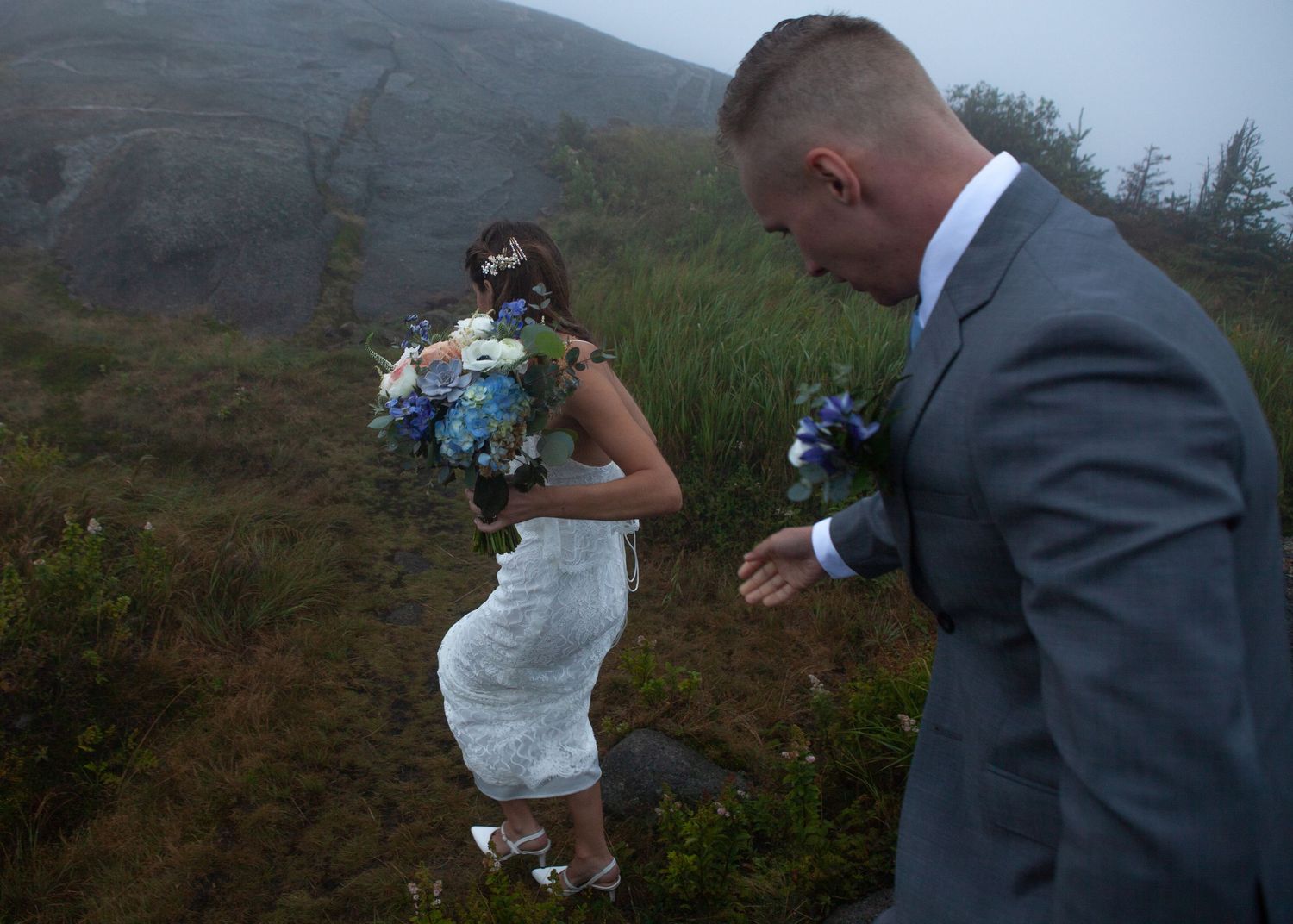A couple dances playfully on a mountain trail with scenic views in the background.