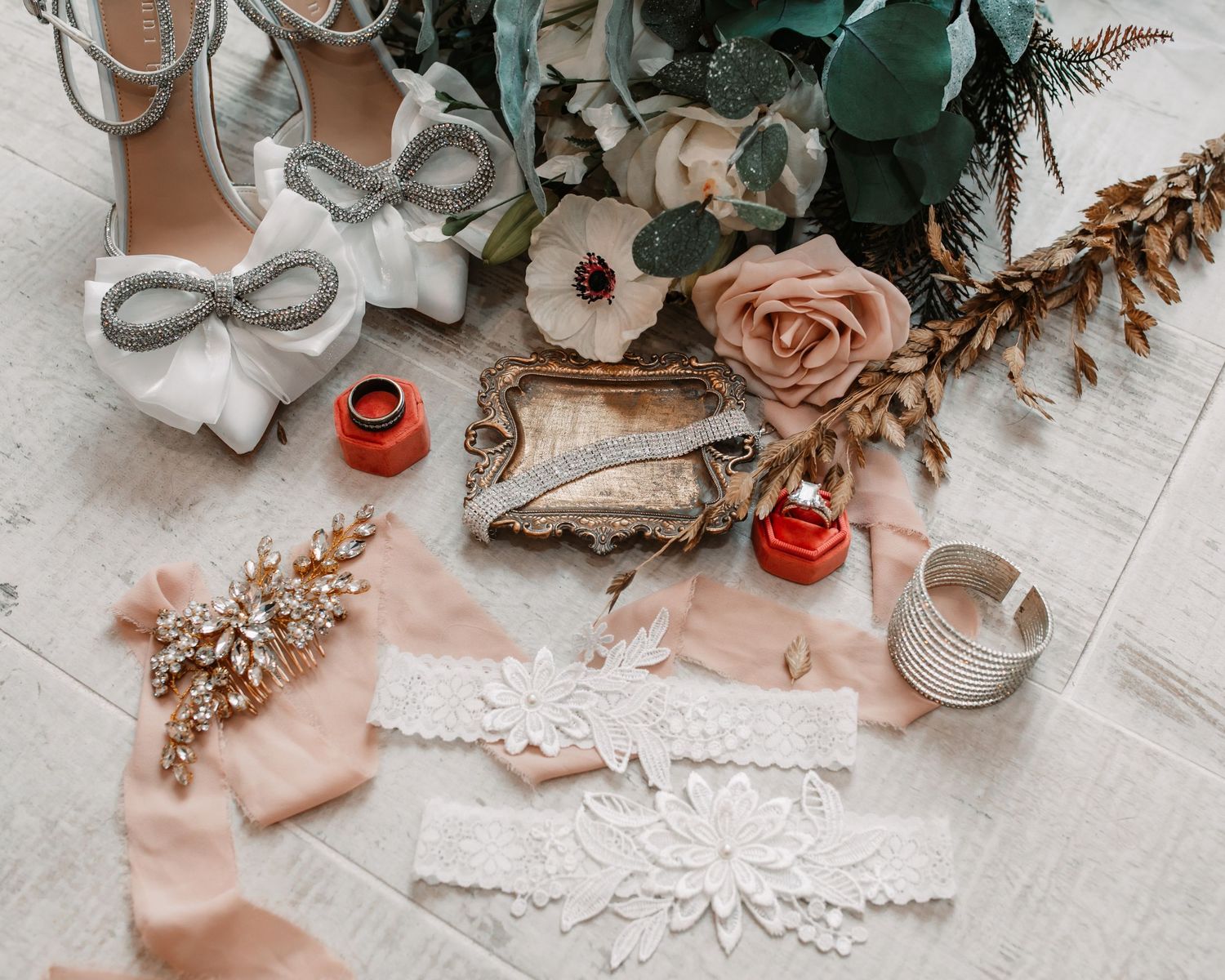 Wedding accessories including bow shoes, lace garter, and floral decor on light background.