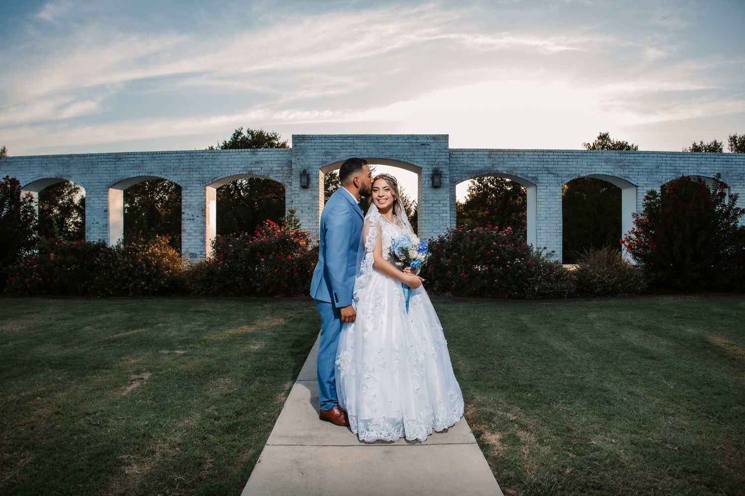 Elegant wedding portraits taken outdoors with white columns and blue sky in the background.
