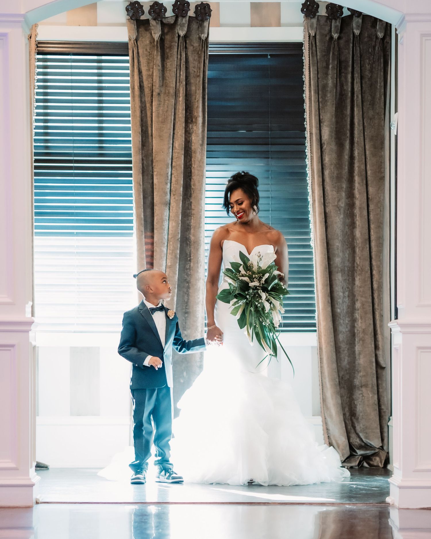 A beautiful first look sequence between mother and son  near large windows with white curtains.