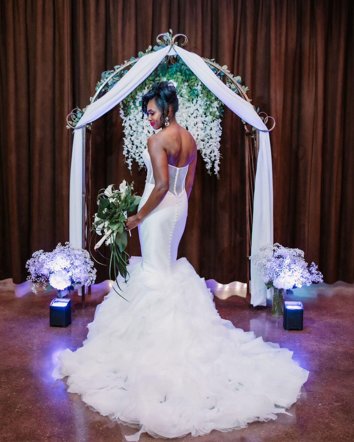 Back view of a white wedding gown with dramatic train under decorative floral arch.