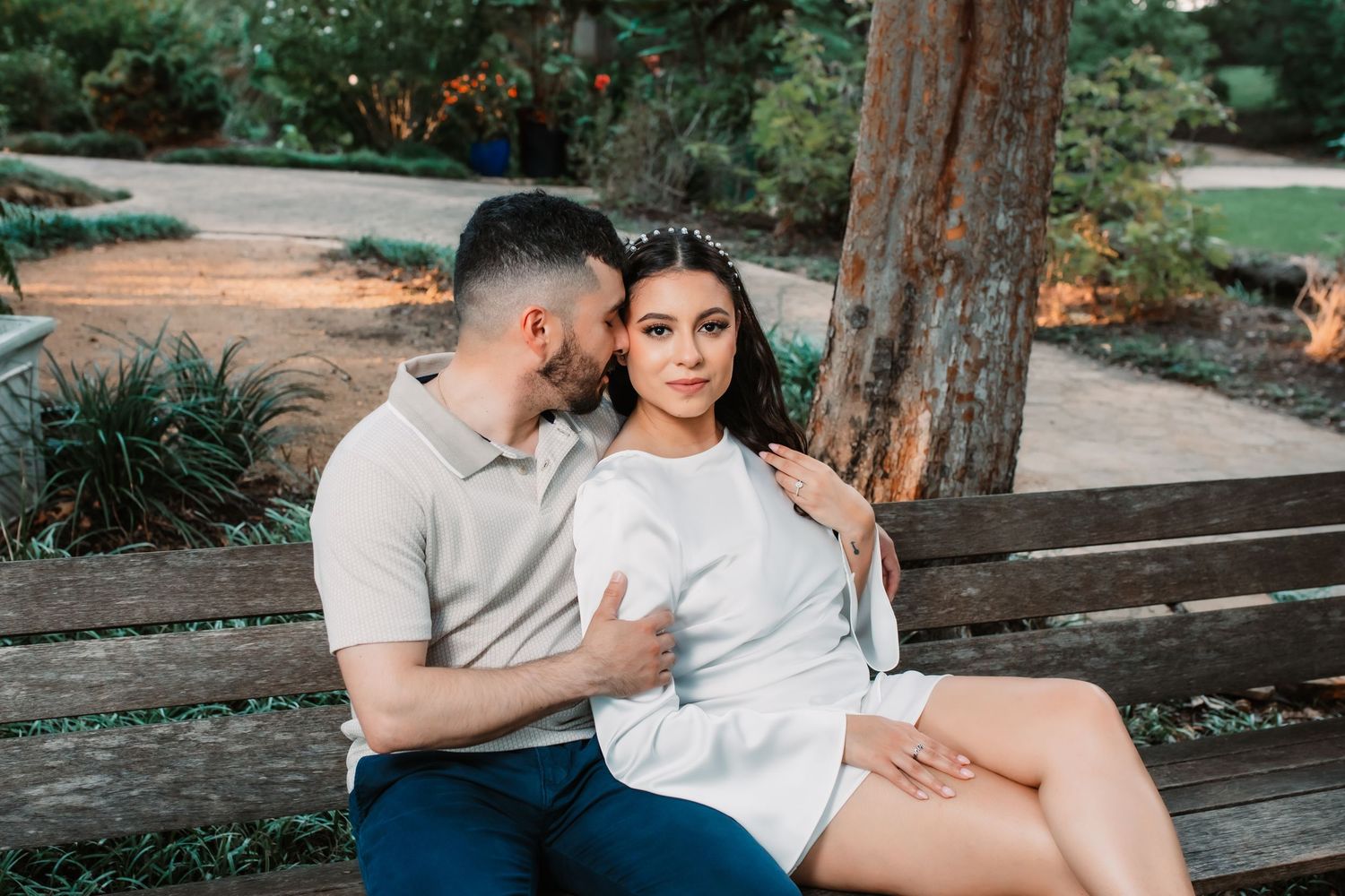 Romantic engagement photos on rustic wooden bench in park setting.