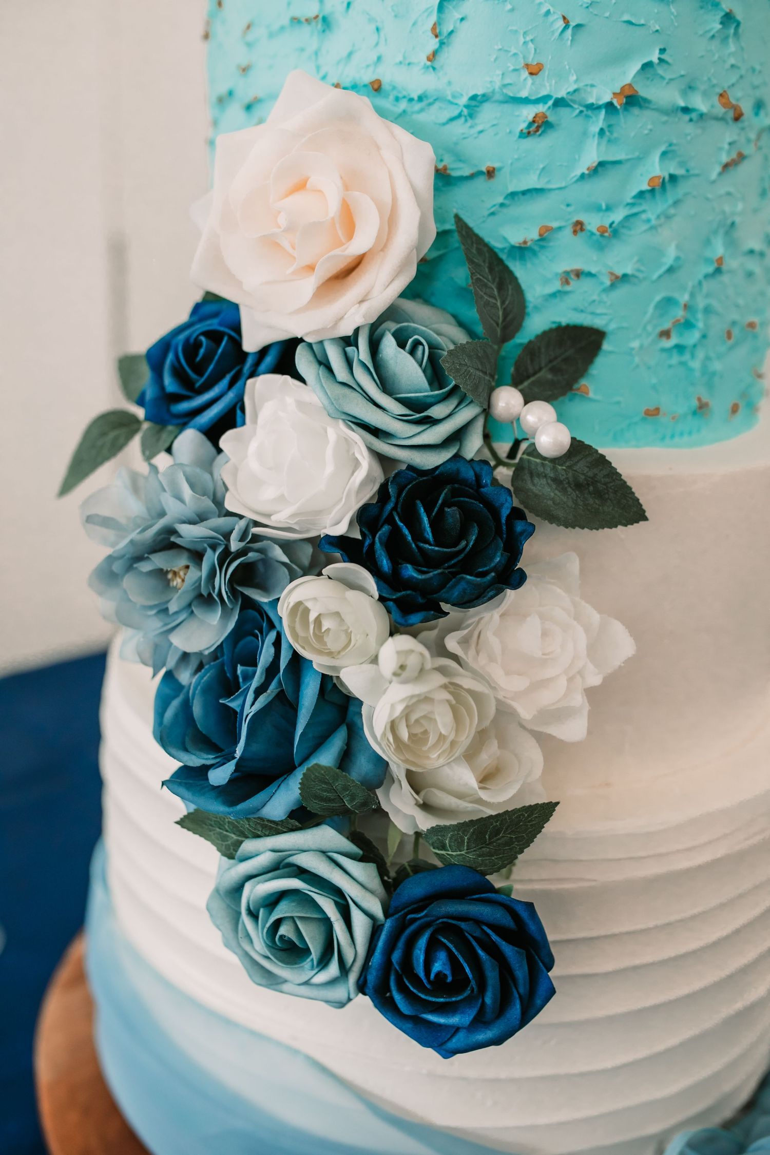 Wedding cake decorated with cascading blue and white sugar roses against turquoise background.