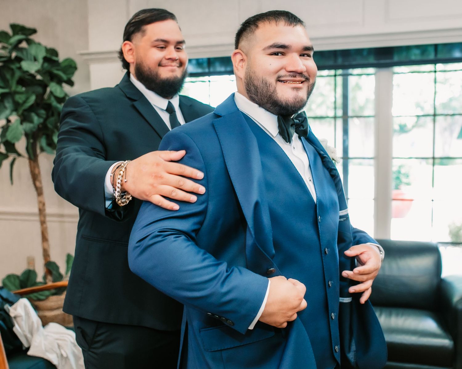 Two men in formal suits share a joyful moment while getting ready for a wedding ceremony.