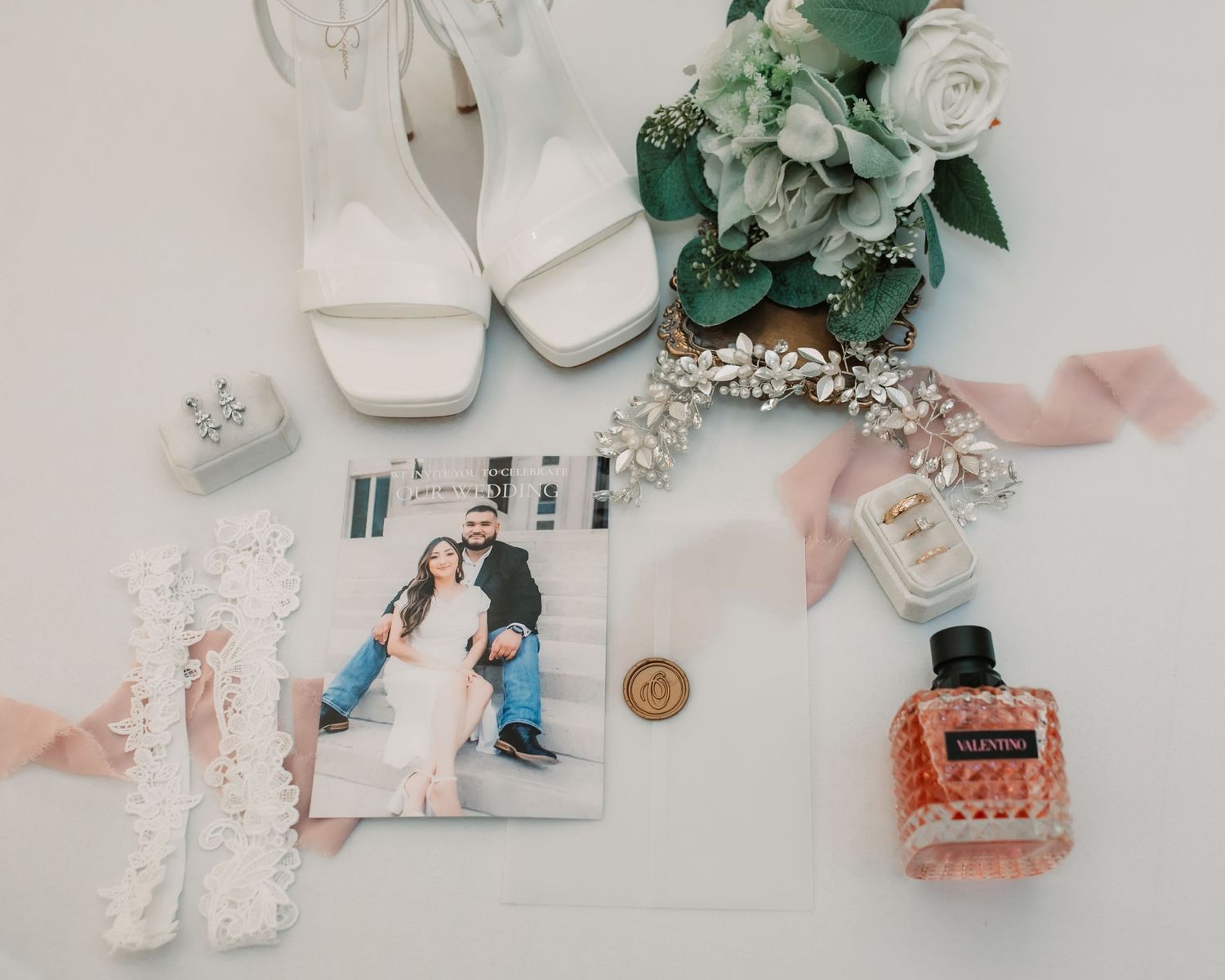 Wedding detail flatlay with white shoes, greenery, and invitation suite on light background.