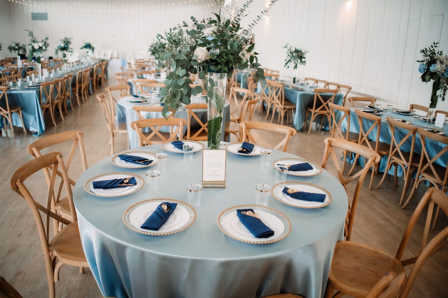 Wedding reception tables decorated in soft blue and white with cross-back chairs.