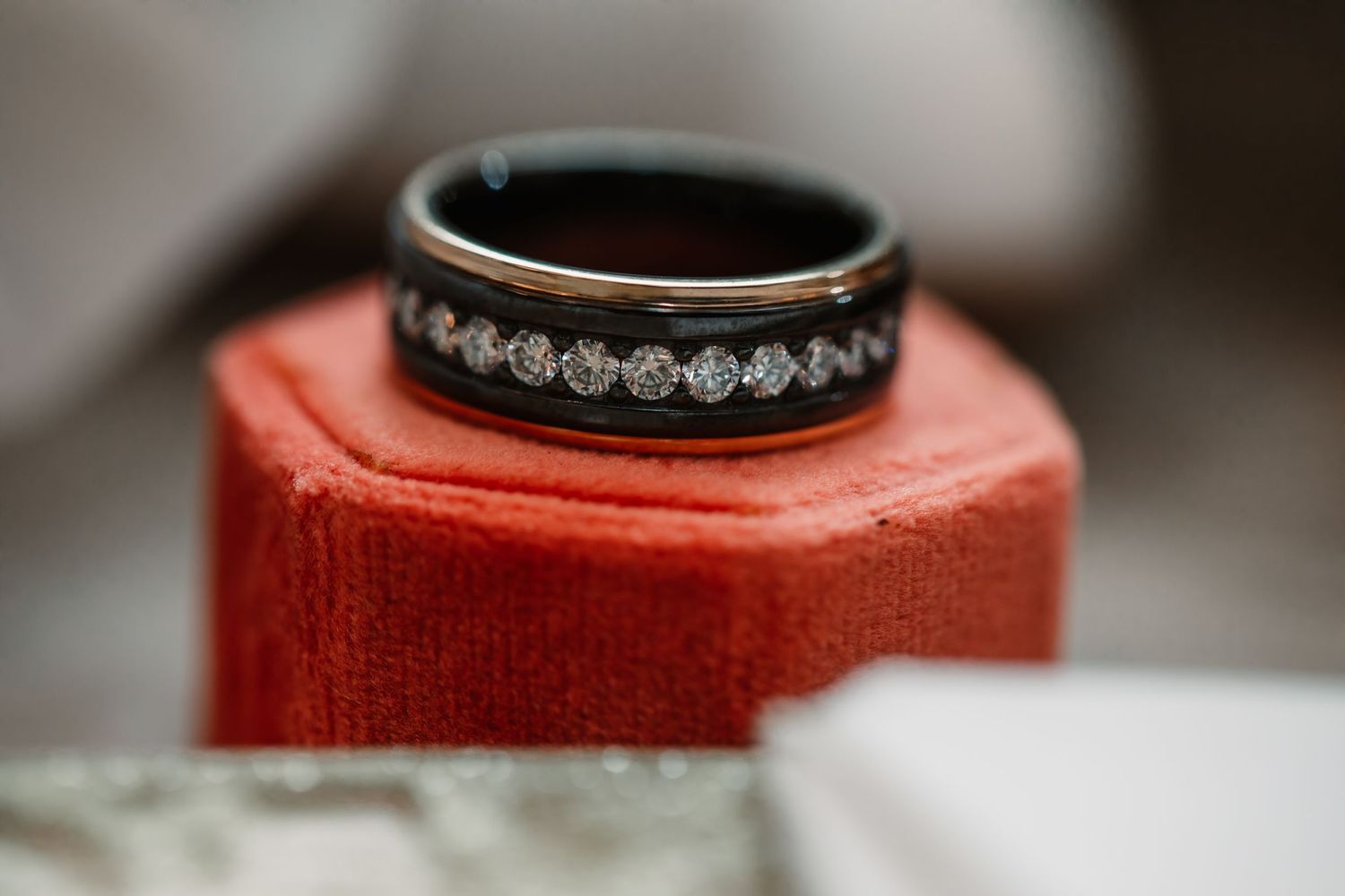 Black wedding band with diamond accents displayed on red velvet ring box.