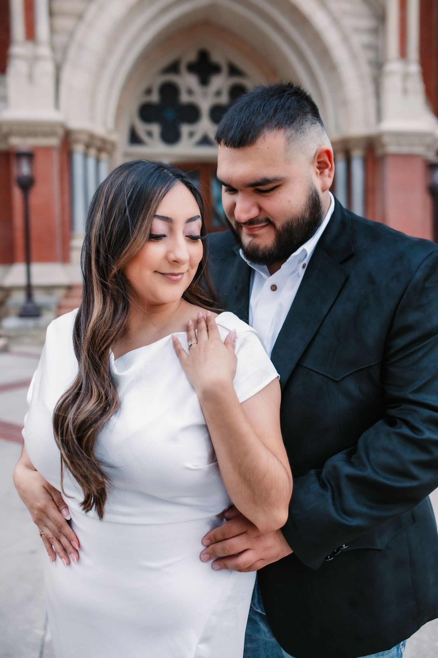 Romantic couple in formal attire posing against an ornate architectural backdrop.