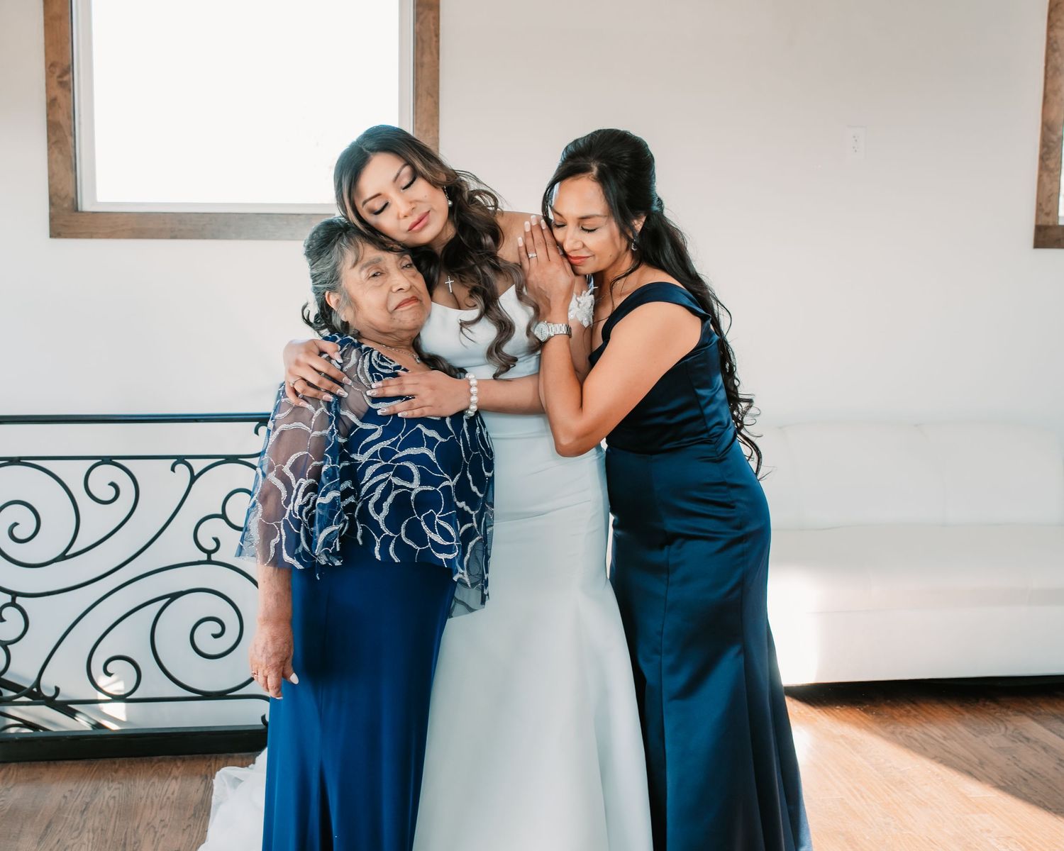 Bridesmaids in navy blue dresses share emotional moments with bride in white gown.