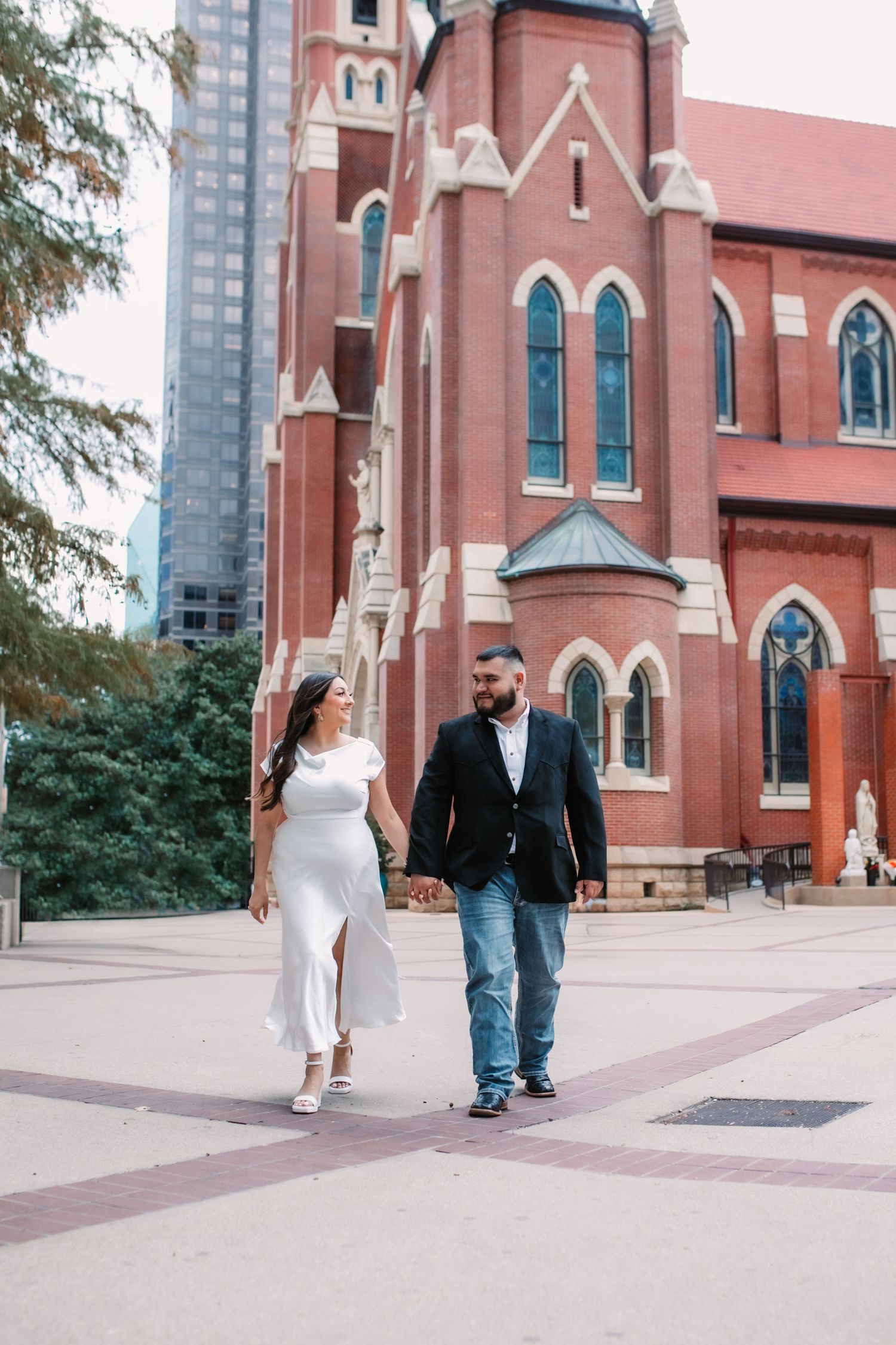 Couple walking together outside a red brick church with gothic architecture.