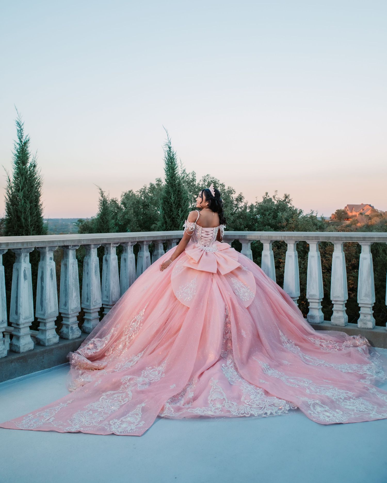 A stunning pink ballgown with a dramatic train photographed on a balcony at sunset.