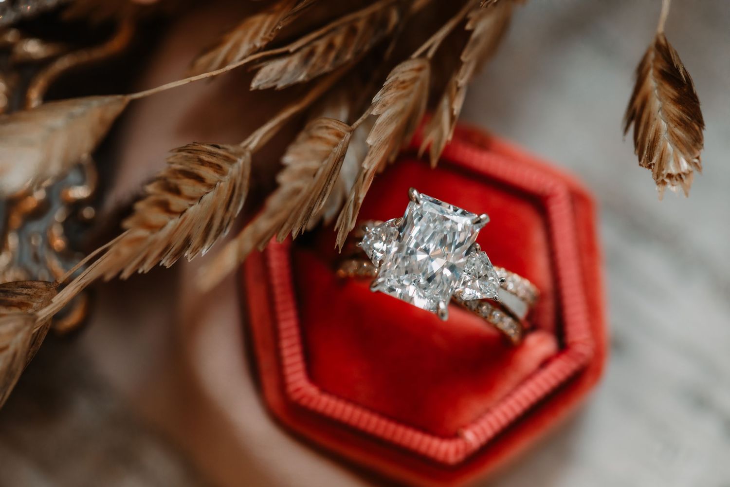 Diamond engagement ring in red velvet box with dried wheat stems.