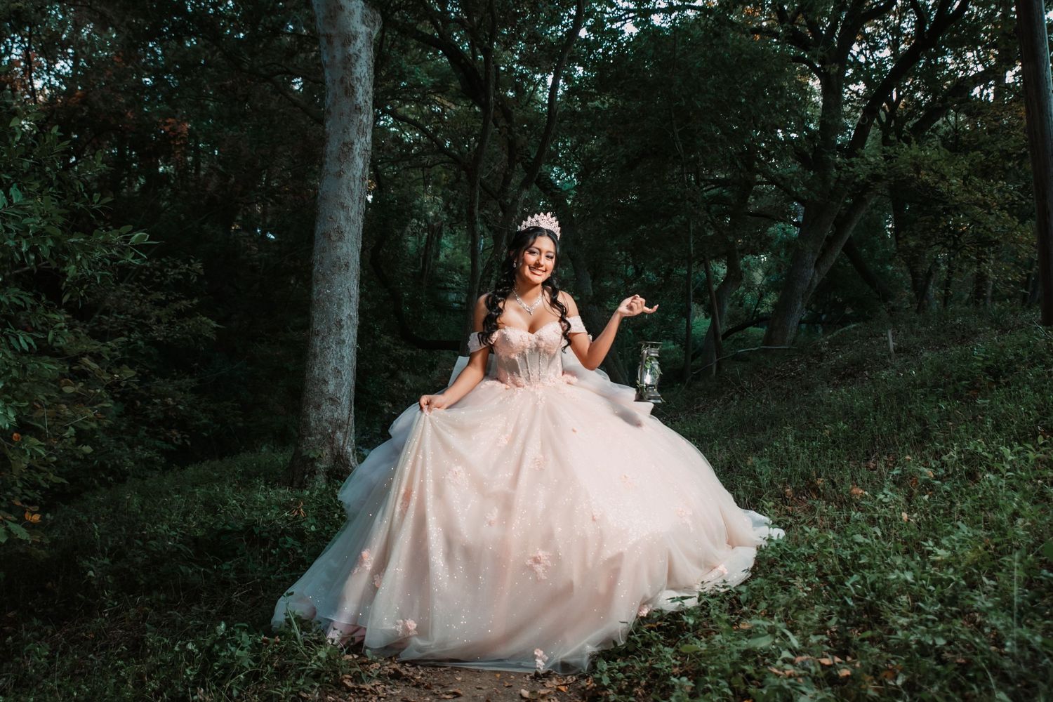 A Quinceañera in a flowing ballgown twirls playfully in a wooded outdoor setting.