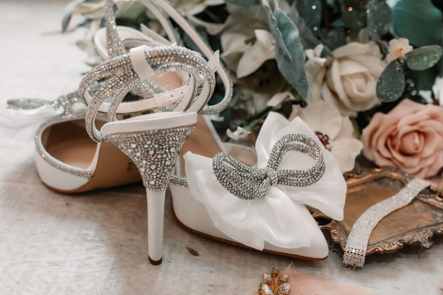 Crystal-embellished bridal heels with bow detail and floral backdrop.