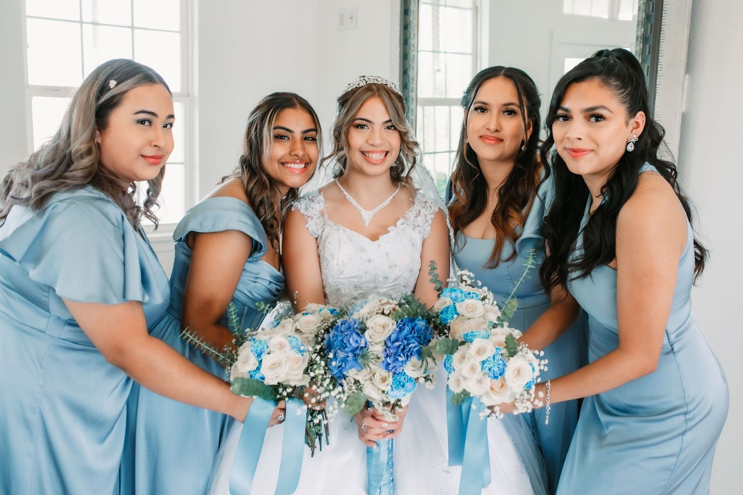 Bridesmaids in light blue dresses posing together in a bright indoor venue.