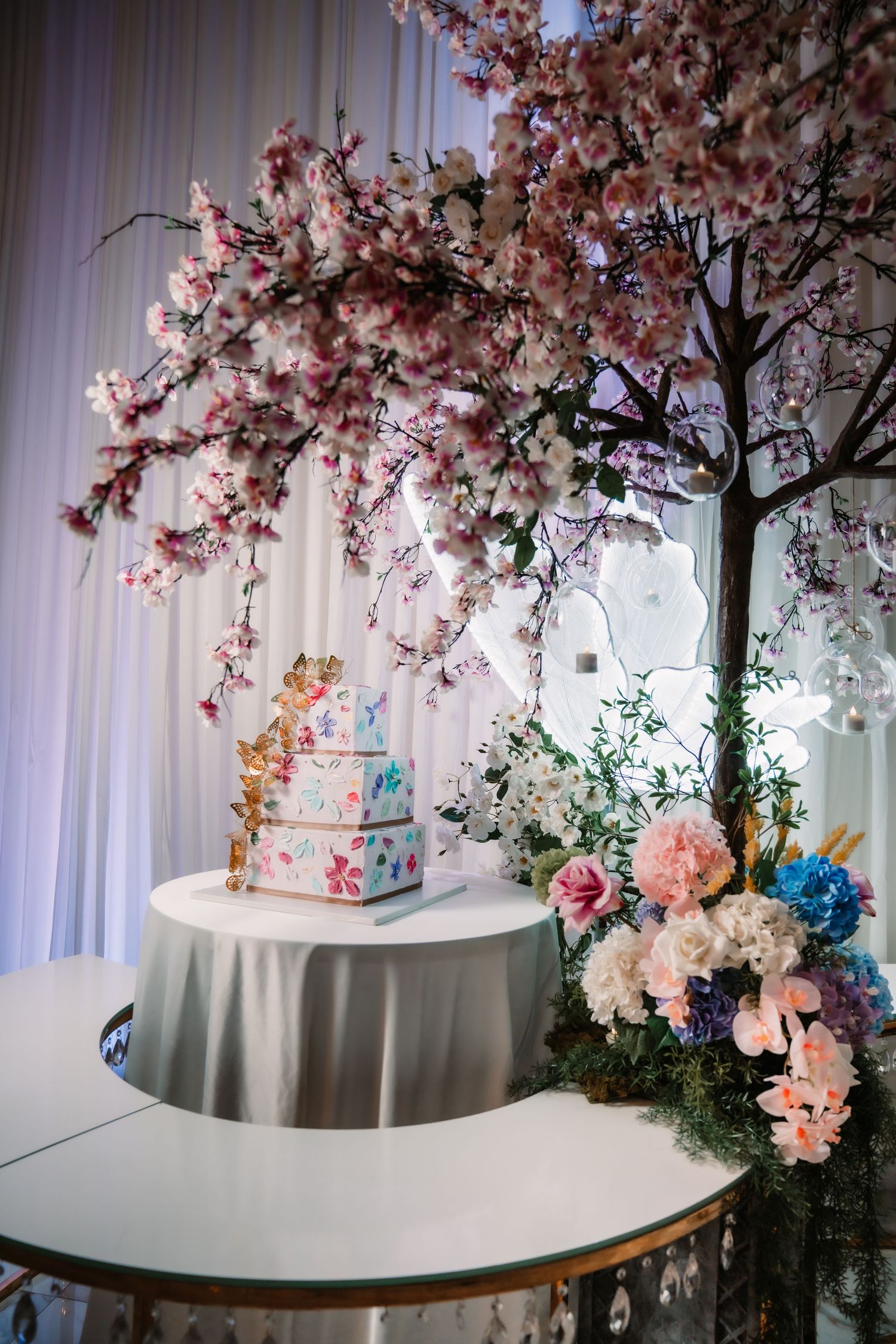 Elegant wedding reception decor featuring cherry blossom trees and white draping.