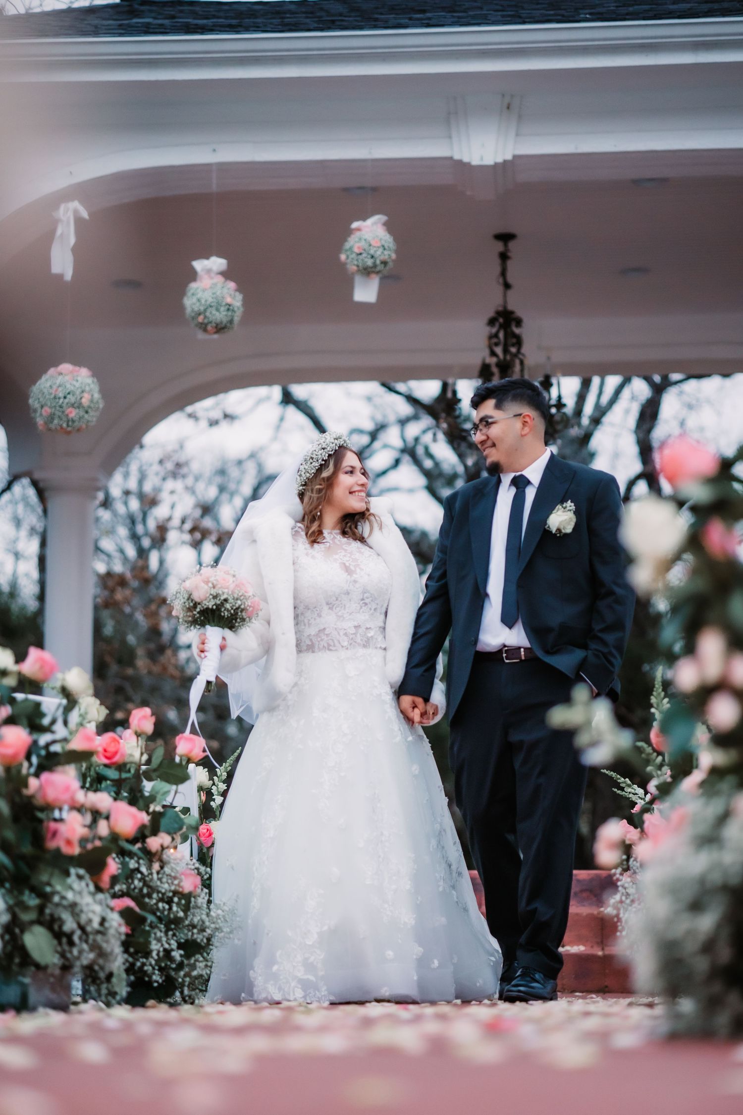 Romantic wedding couple dancing together under a white gazebo decorated with pink roses and floral arrangements.
