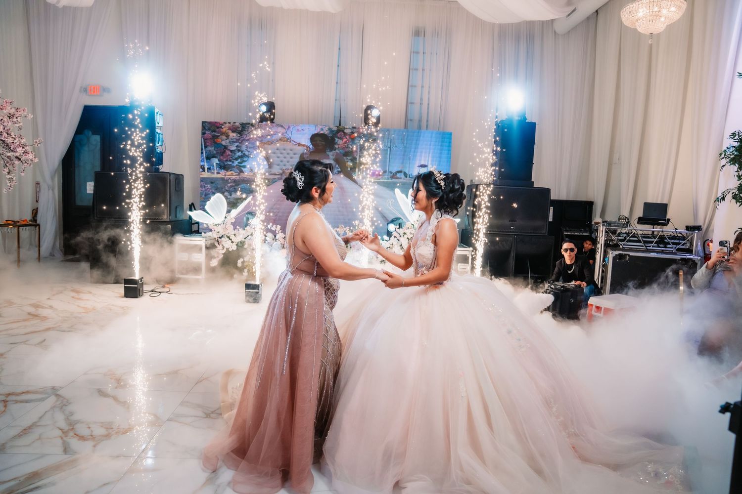Quinceañera venue decorated in white with chandeliers and romantic lighting creating a dreamy atmosphere.