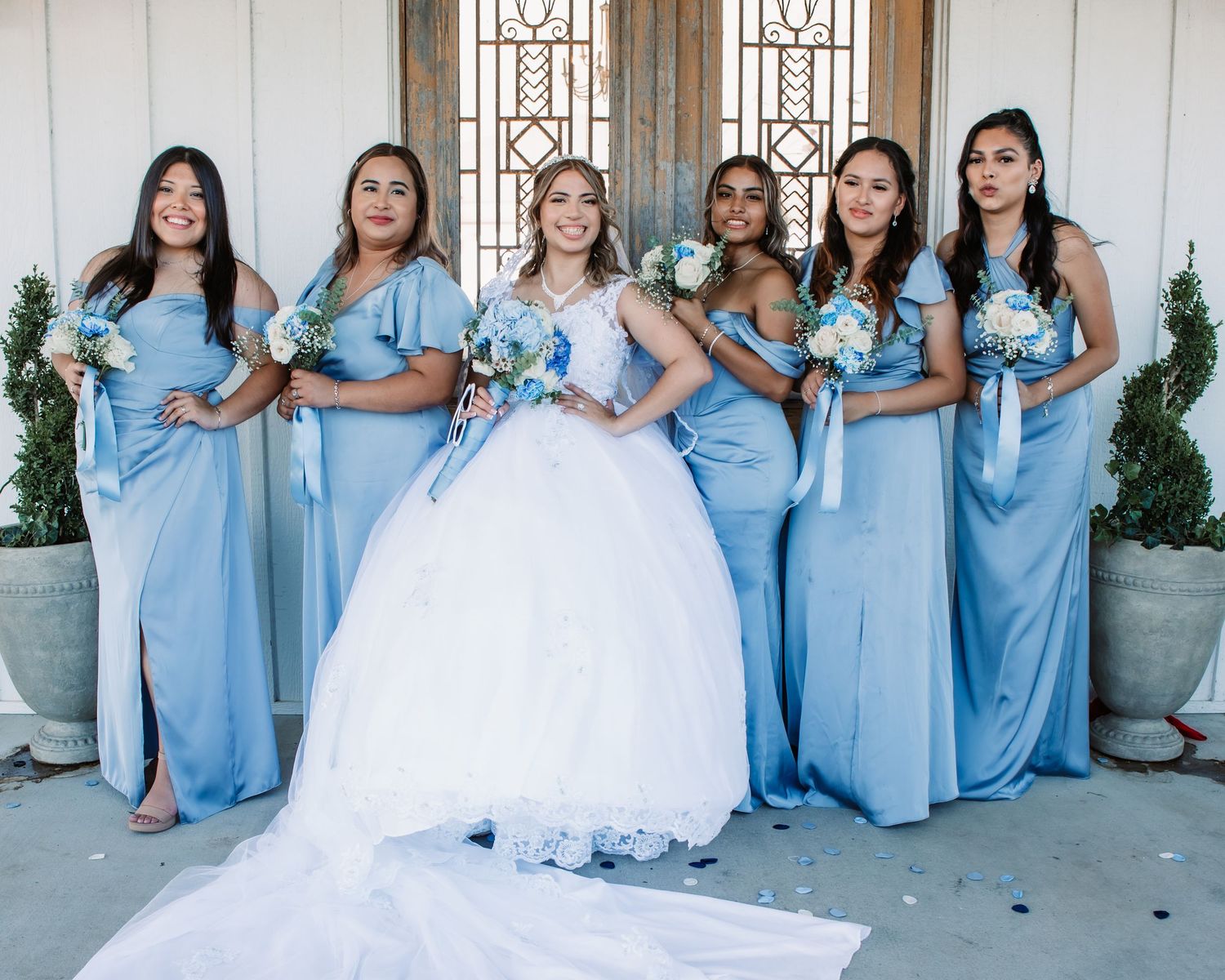 Bridal party in light blue dresses gathered around bride in white gown.
