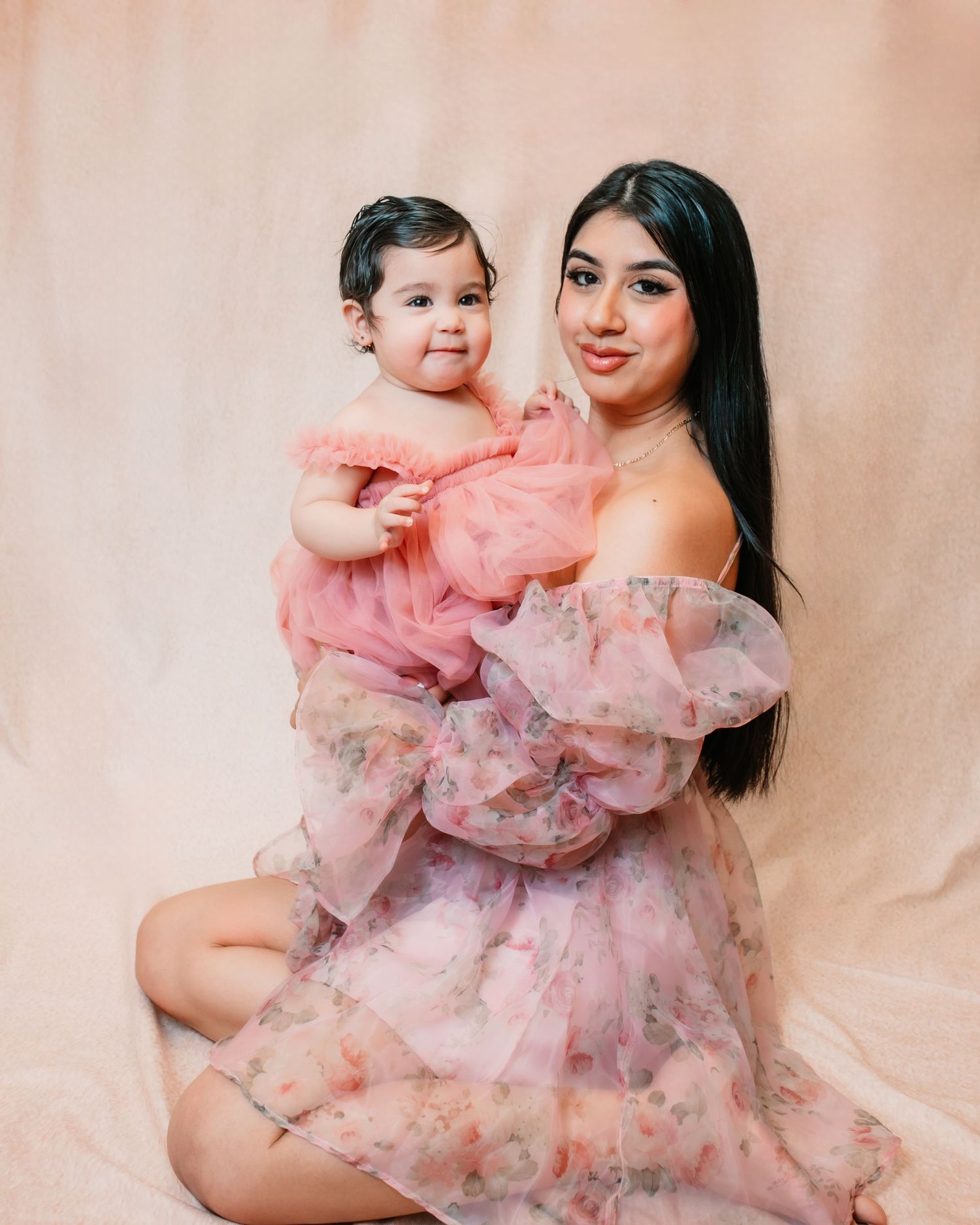 A sweet portrait session featuring matching pink and floral dresses against a beige background.
