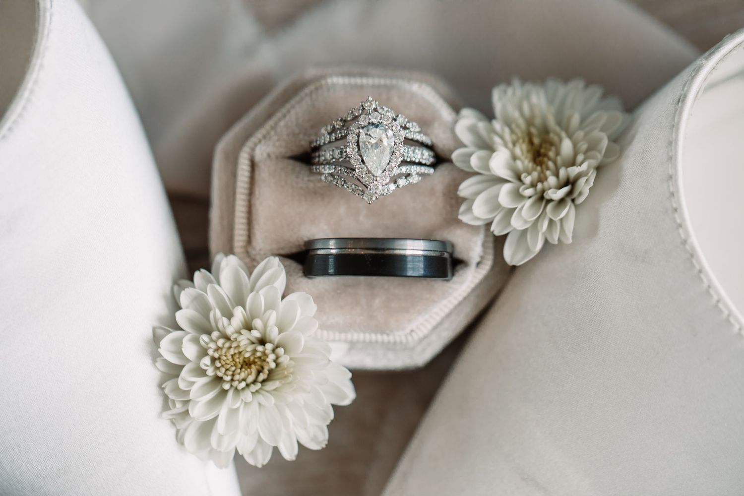 White wedding flowers and diamond engagement ring displayed on a light beige surface.
