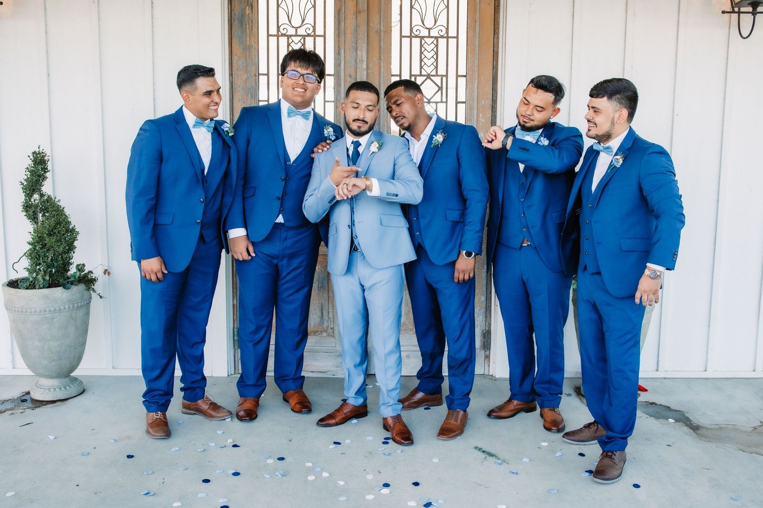 Groomsmen in various shades of blue suits sitting together on outdoor porch.