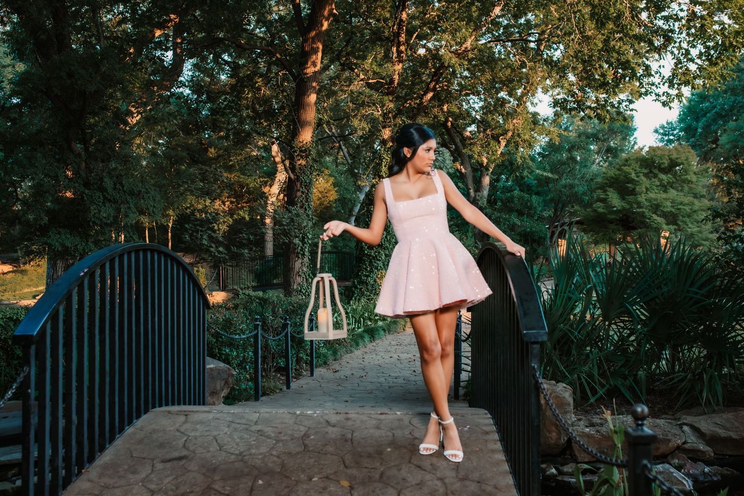 A person in a pink dress walks along an outdoor path surrounded by trees and railings.