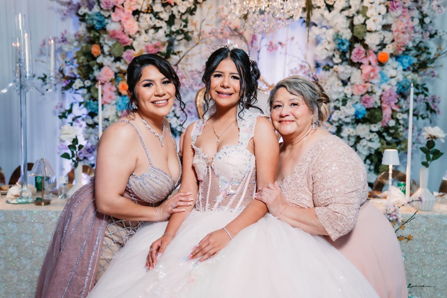 Quinceañera party in pink and blush dresses posing together with floral decorations in the background.