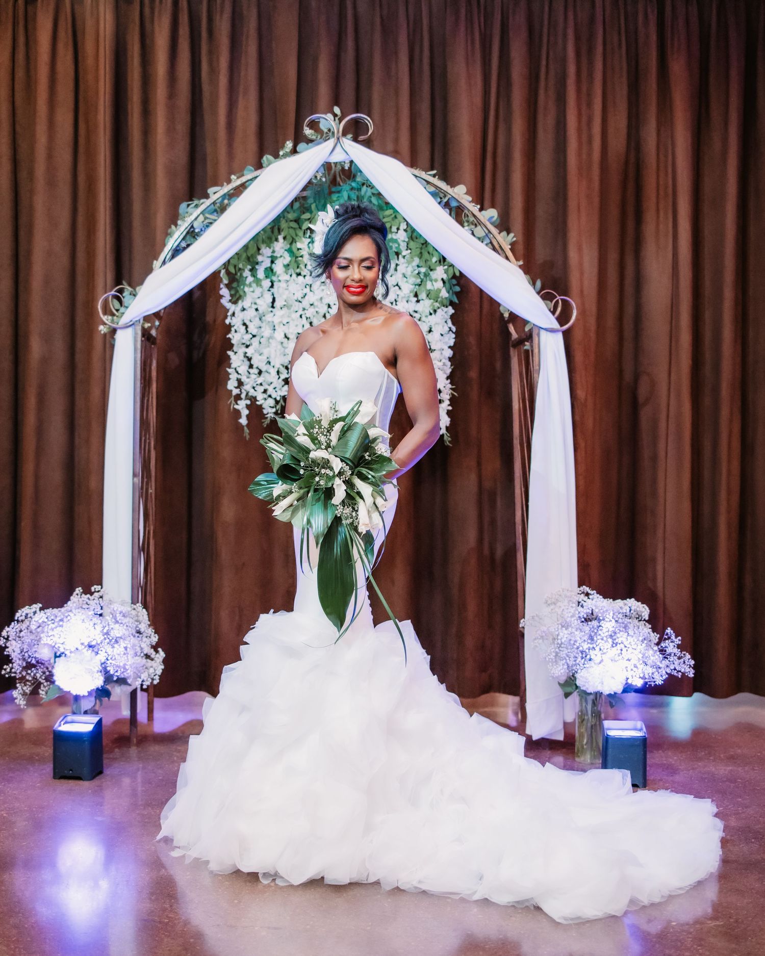 A stunning bridal portrait under a floral arch with purple uplighting and white draping.