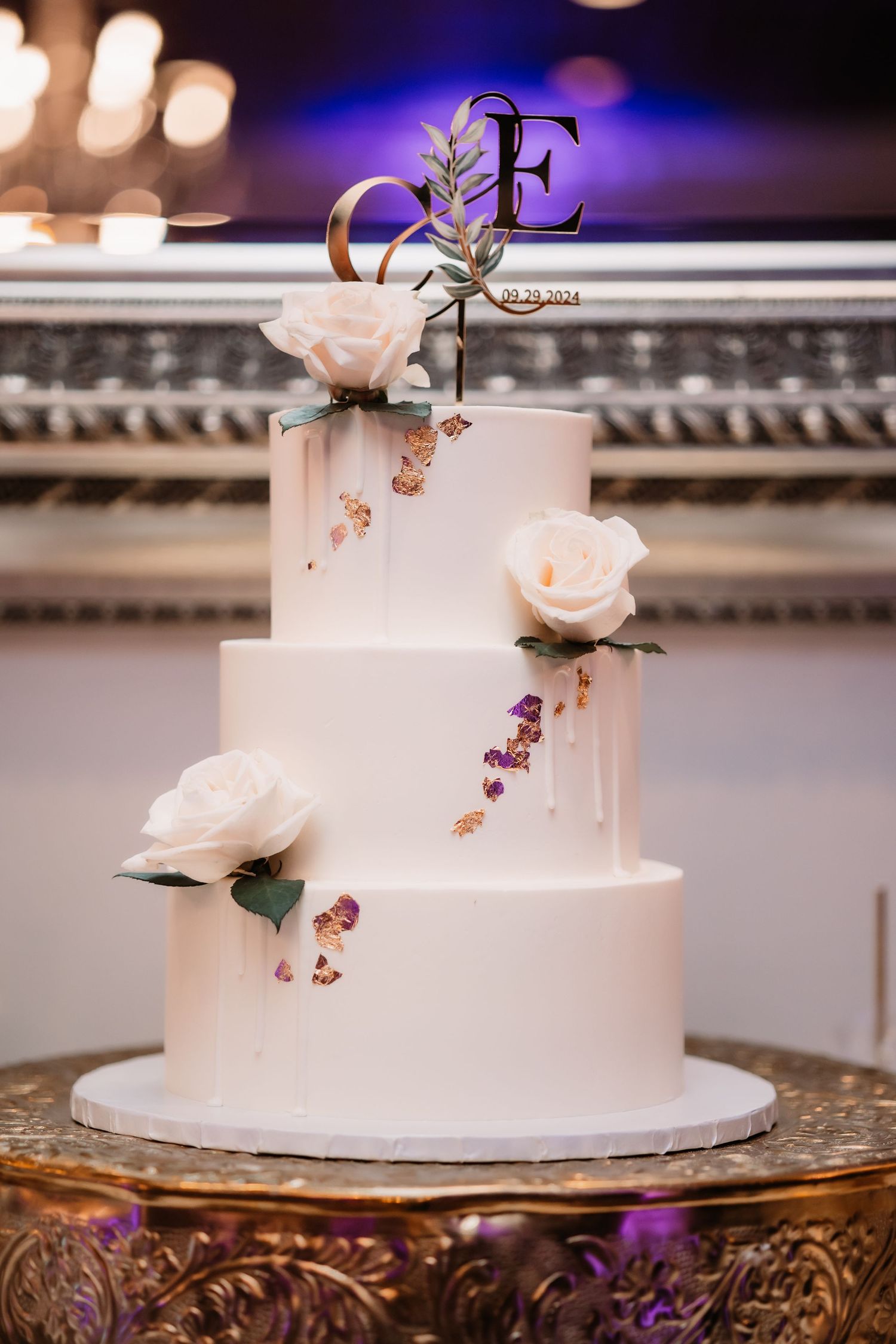 Elegant white wedding cake with monogram topper displayed on ornate gold stand.