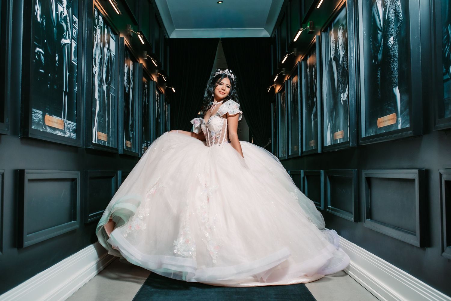 A dramatic quinceanera portrait in a dark hallway with elegant navy blue walls.
