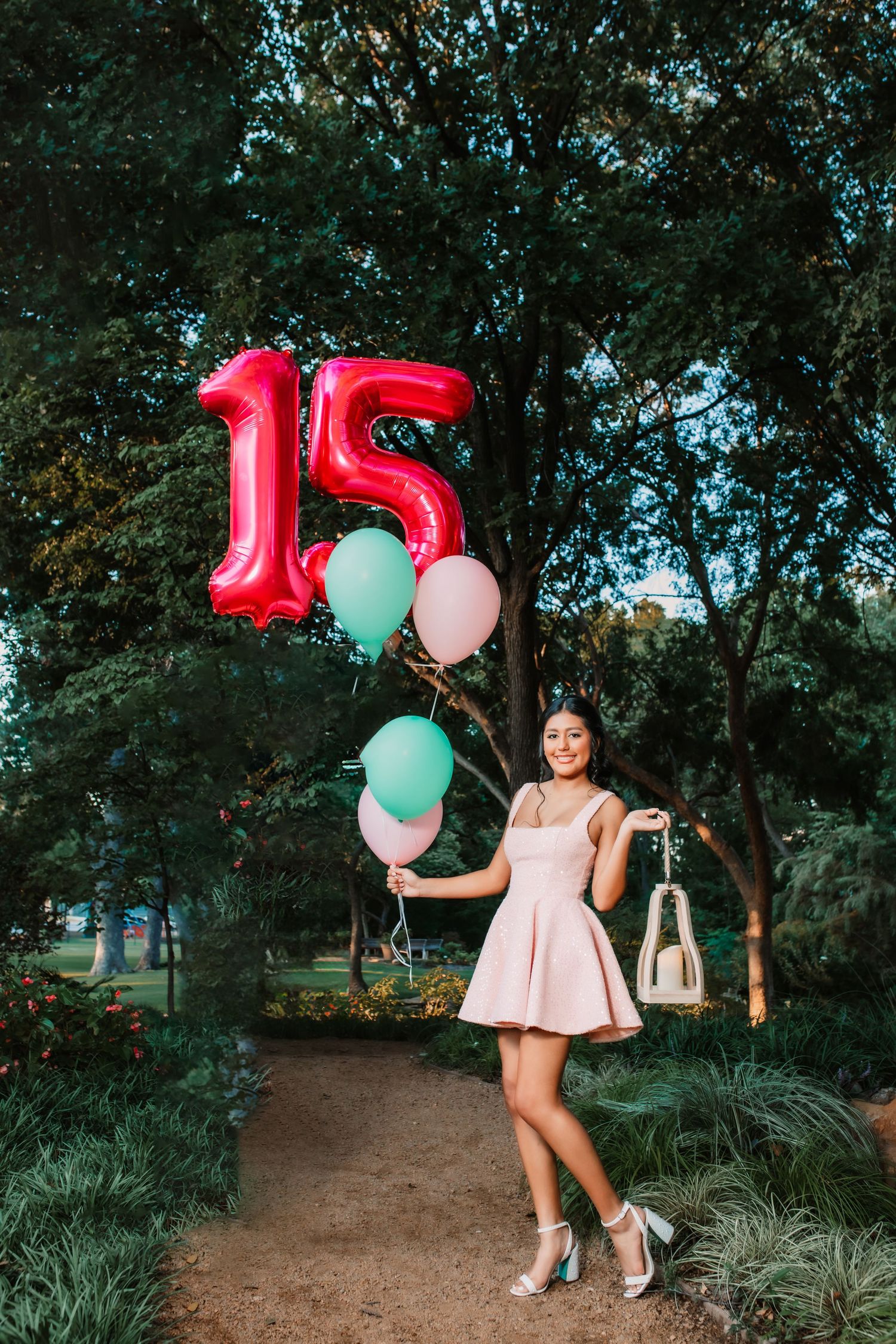 A celebratory scene with pink and mint green balloons on a tree-lined path.