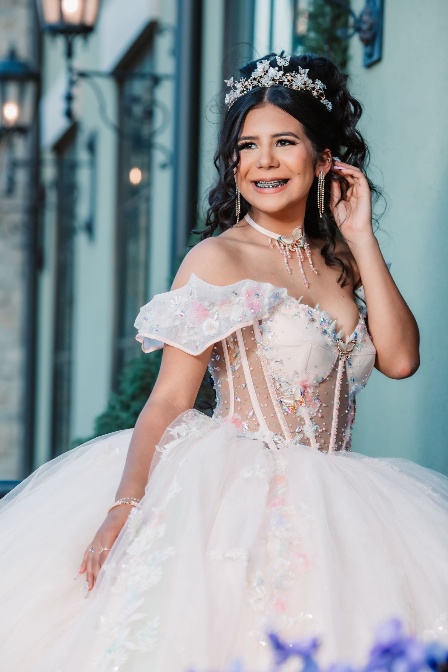 A bride in a sheer corset ballgown poses beside blue-tinted windows and stone walls.
