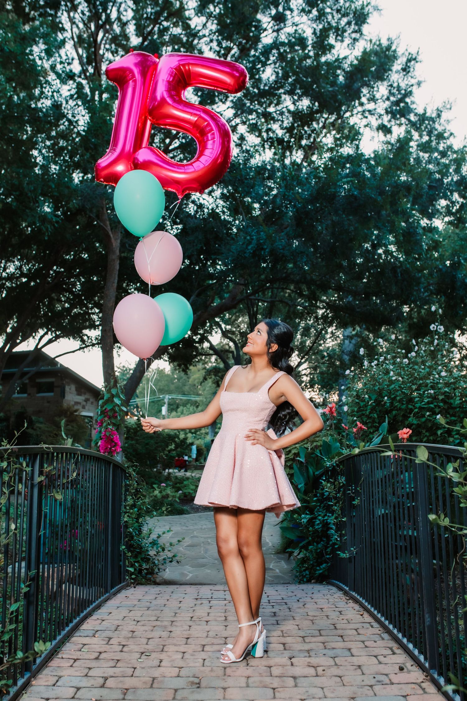 A celebration photoshoot with number 15 balloons and a pink dress on a stone pathway.