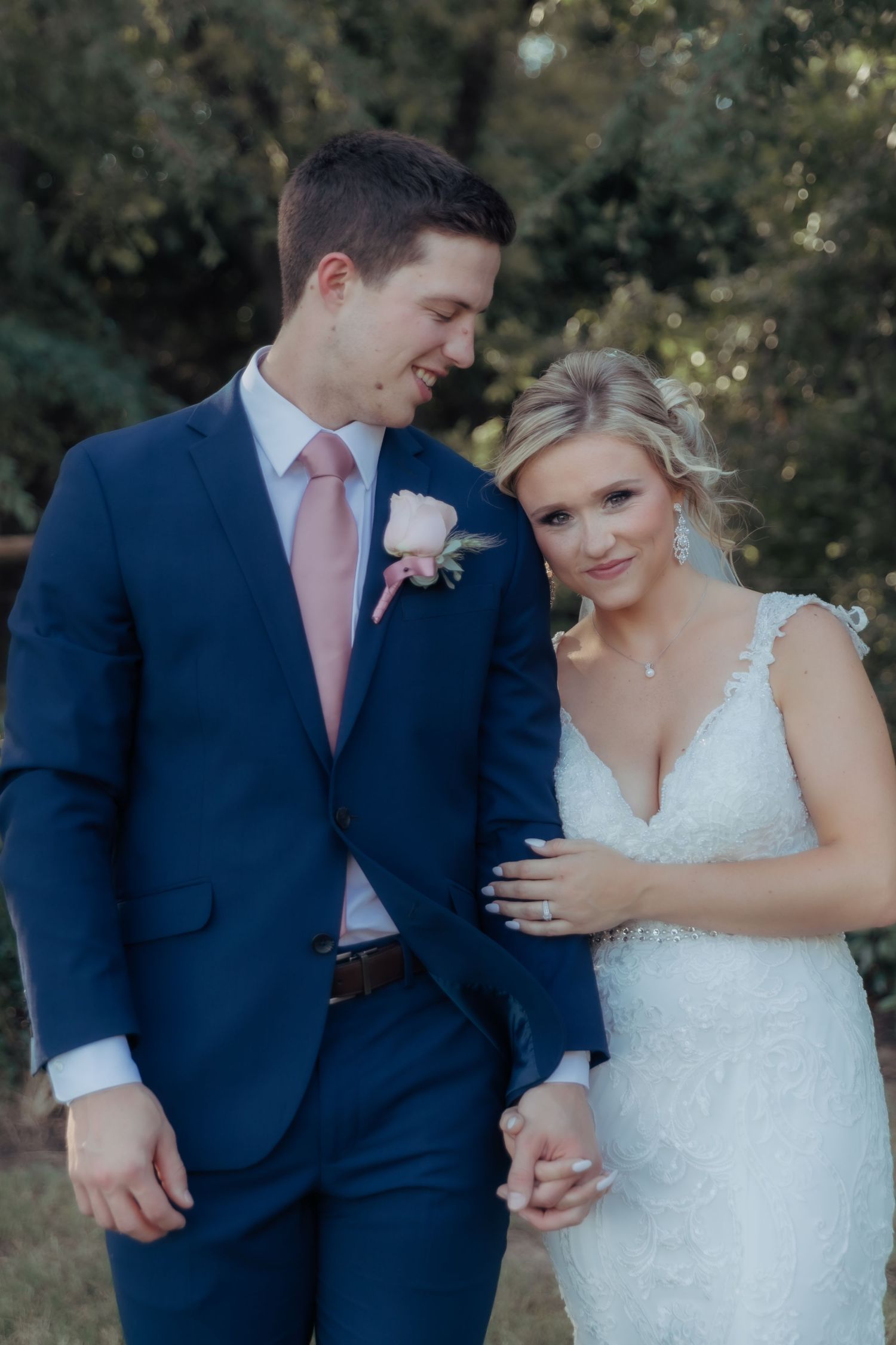 A romantic wedding couple in navy suit and white lace dress share intimate moments in an outdoor photoshoot.