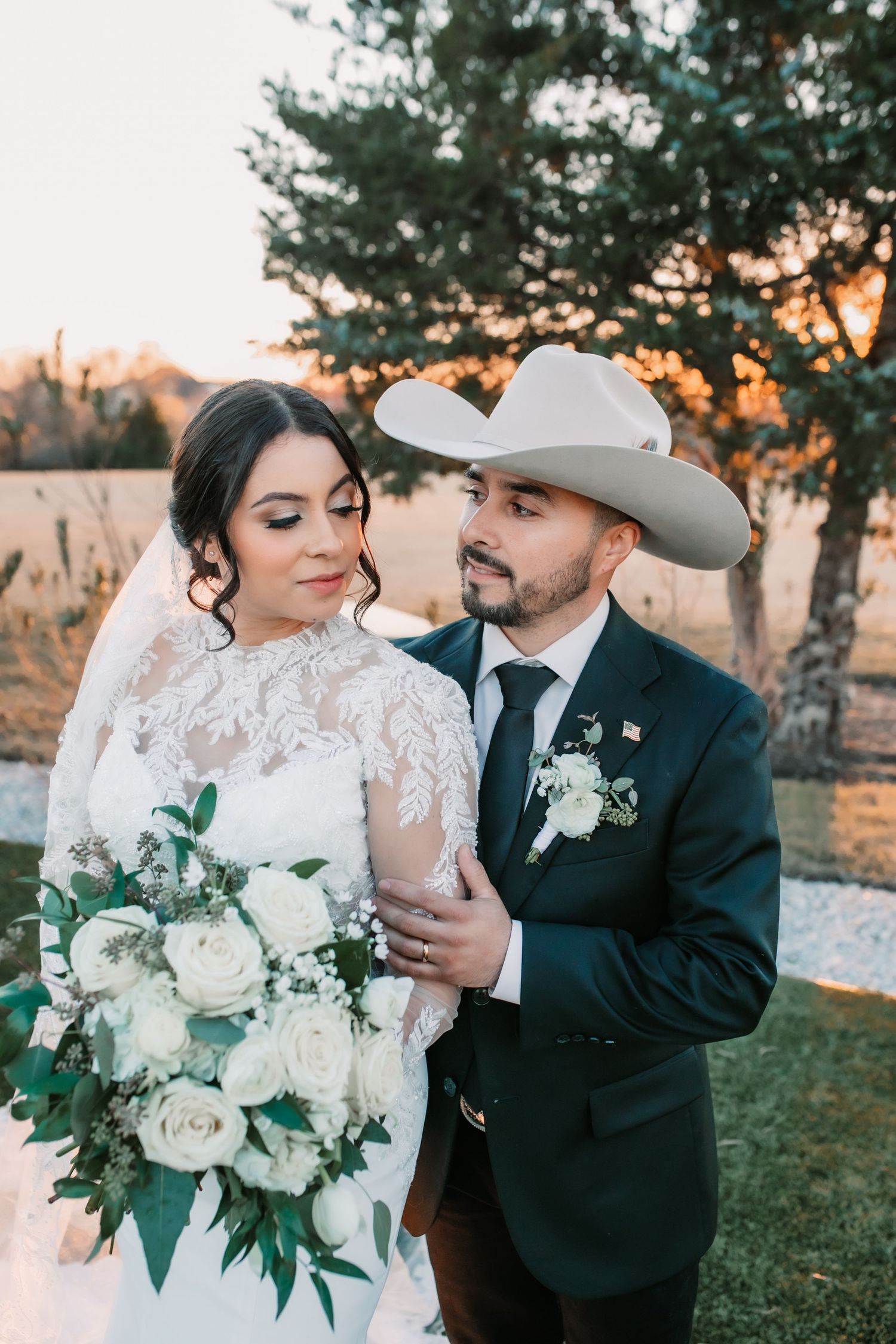 Romantic wedding portraits with white rose bouquet against sunset backdrop.
