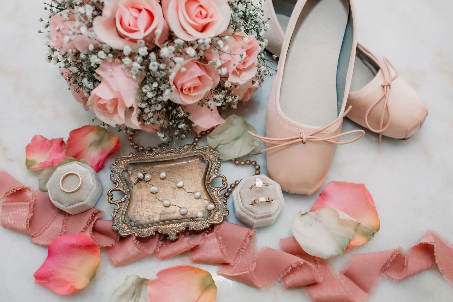 Pink roses bouquet with ballet shoes, vintage frame, and scattered rose petals arranged on light background.