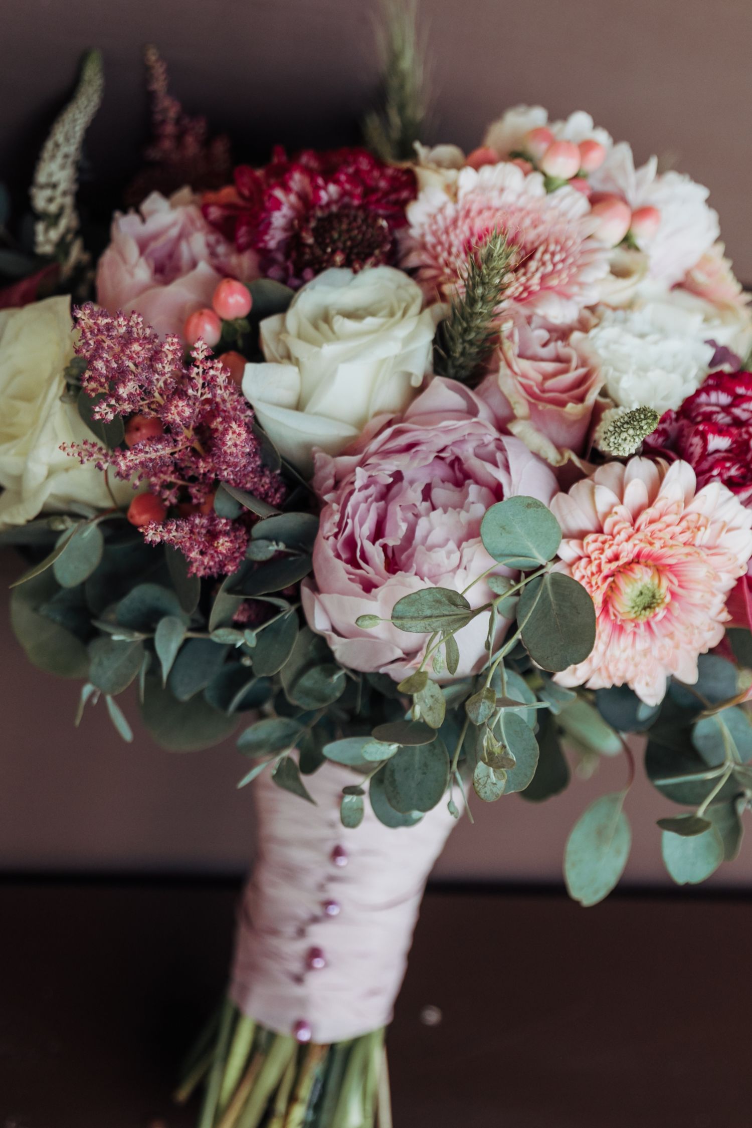 A romantic wedding bouquet featuring pink and white flowers with eucalyptus leaves wrapped in birch bark ribbon.