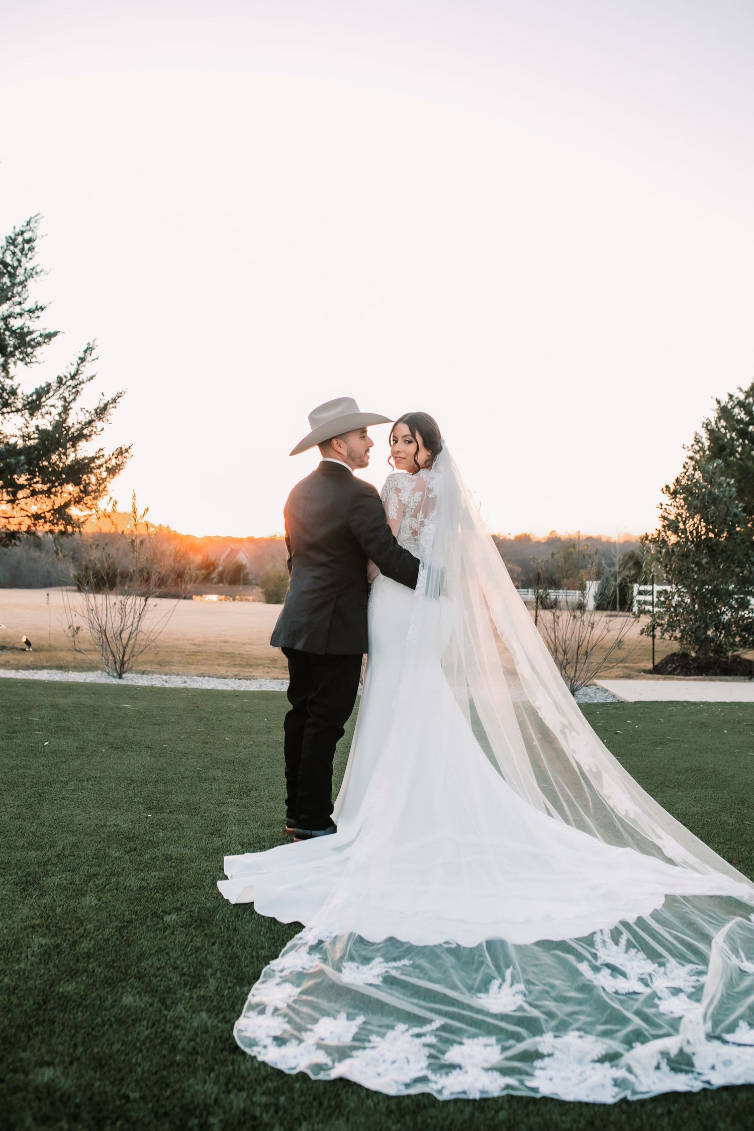 Dramatic wedding dress train spread out on green lawn during sunset photoshoot.