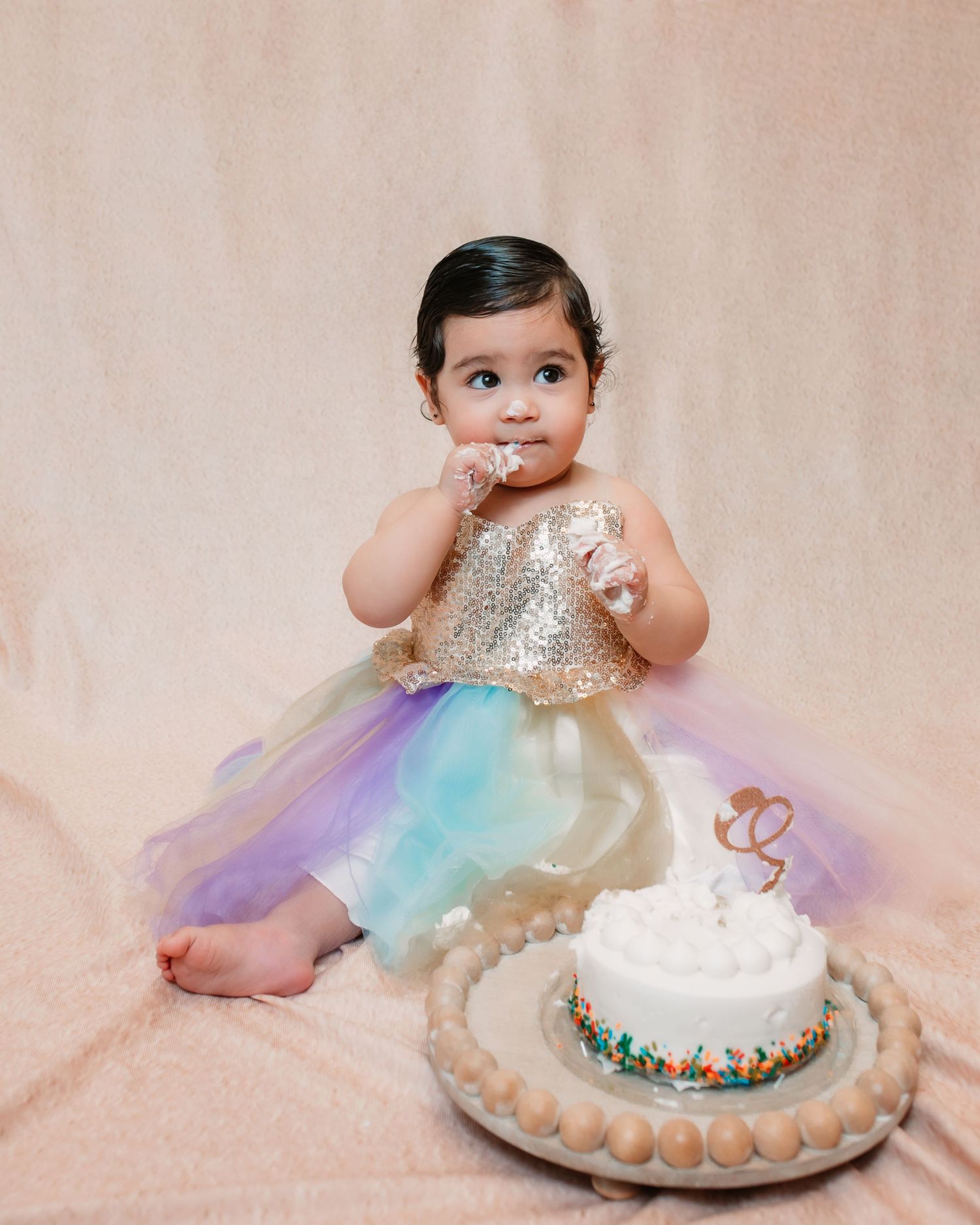 A cake smash photo session with a sparkly dress and colorful birthday cake.