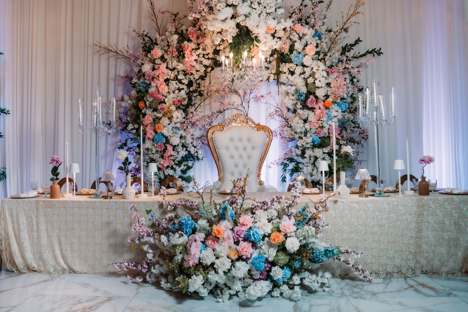 Romantic wedding reception setup with floral arrangements and white fabric backdrop.
